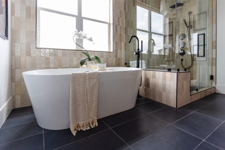 Bathroom with white tiles and a bathtub surrounded by glass shower enclosure.