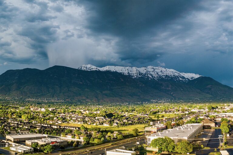 The image shows a cityscape with mountains and clouds in the background.