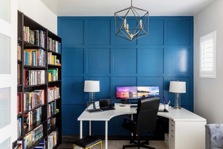 The room is well-lit with natural light and has a modern design featuring bookshelves, desk, computer monitor, and.