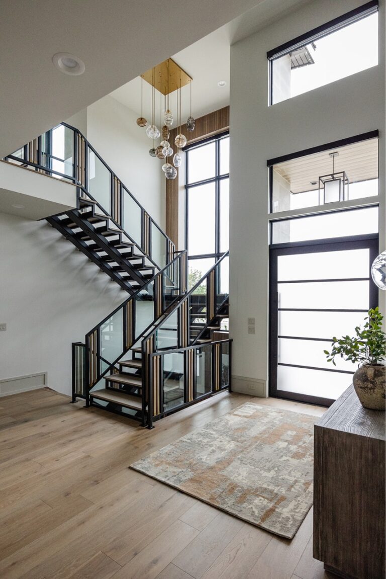 A white room with a staircase and large windows is shown from an angle.