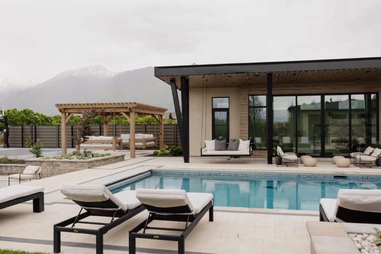 A white-washed photo of a modern house with pool and lounge chairs surrounded by mountains.