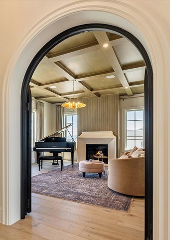 A room with a piano and chandelier is seen through an arched doorway.