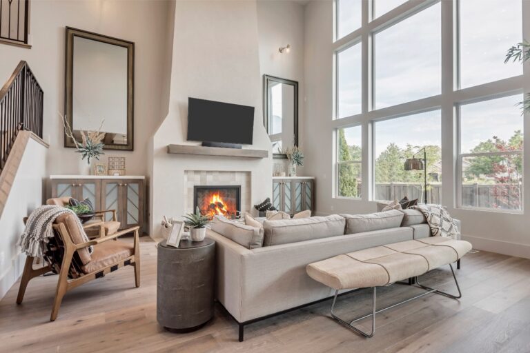 A room with a fireplace and large windows has white walls and furniture.