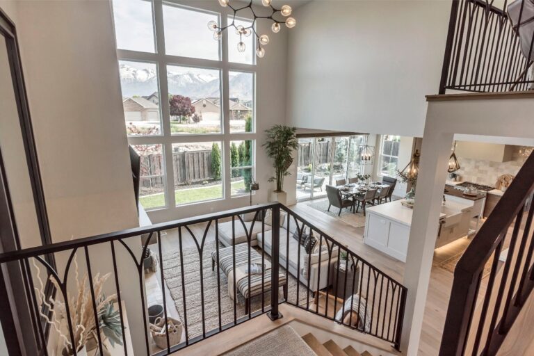 The room is a high-ceilinged space with large windows and chandeliers, featuring an open kitchen area and a.