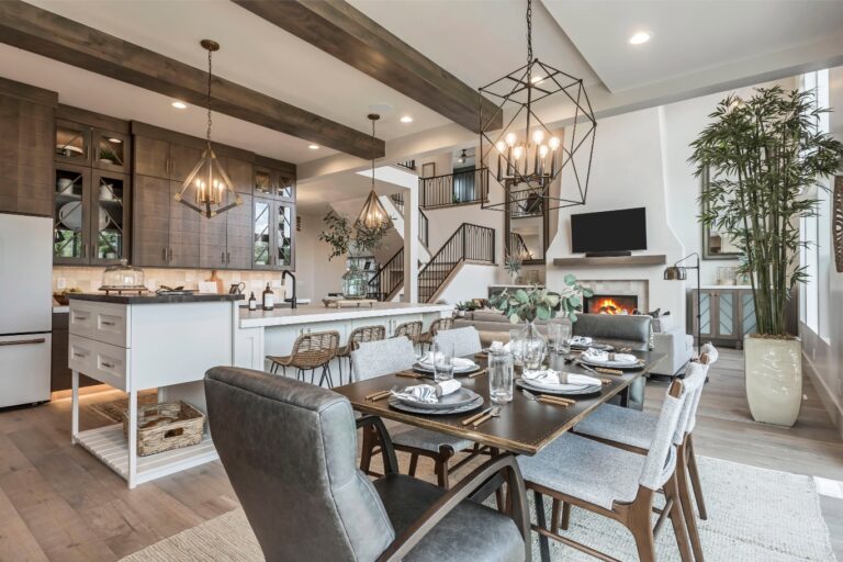 The room is a modern kitchen with white cabinets and wood beams, featuring an island table set for dining.
