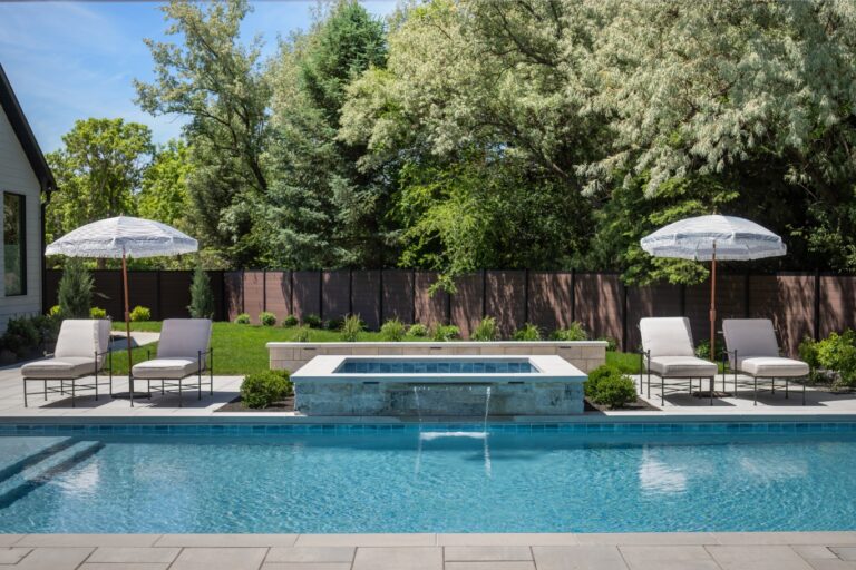 A pool with two umbrellas and chairs surrounded by trees is shown from a high angle.