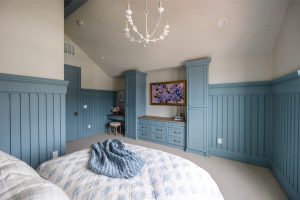 A room with a blue theme and chandelier has two beds and paintings on walls.